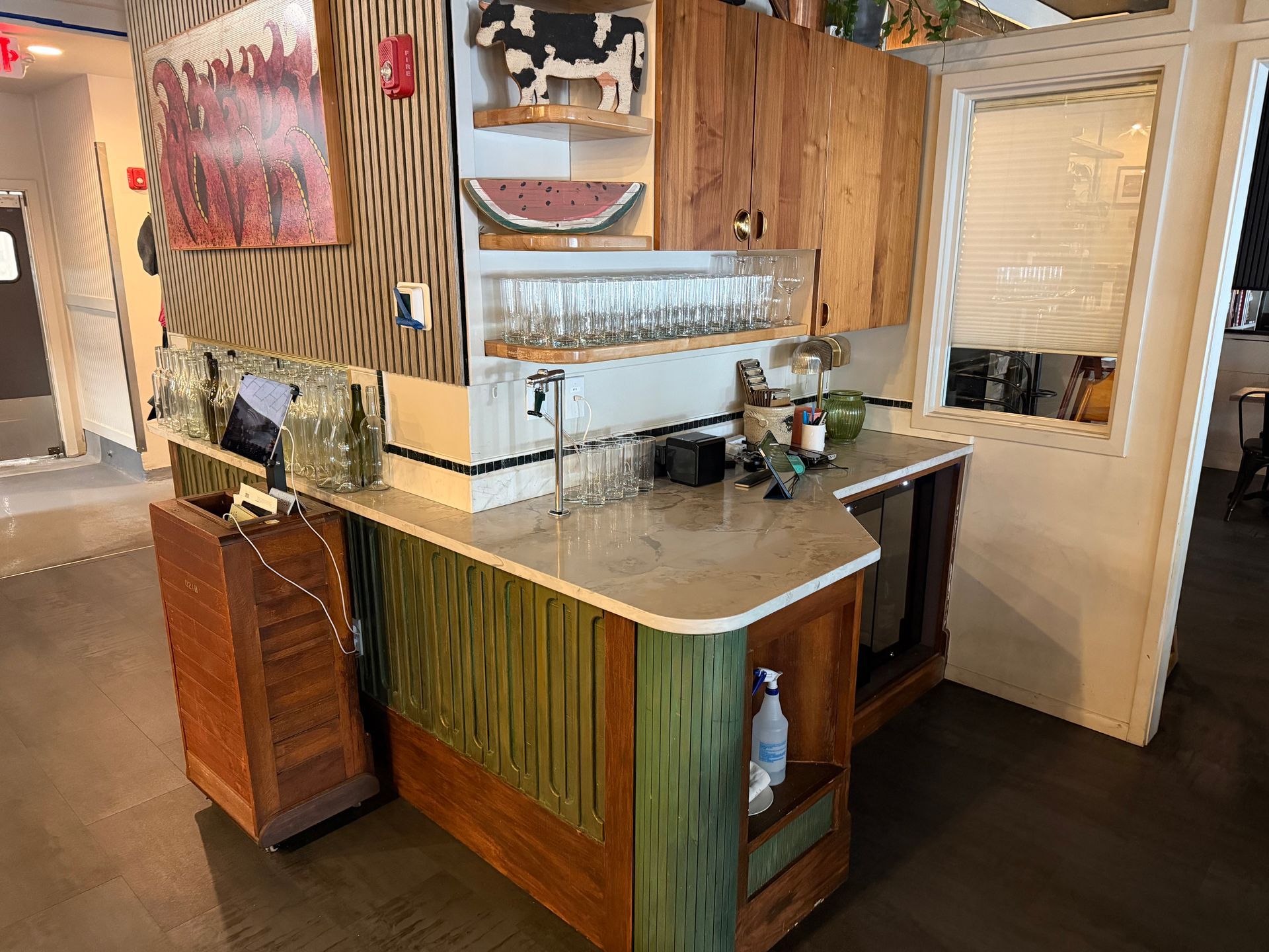 Wood-paneled café counter with sink, coffee machine, and white door in the background.
