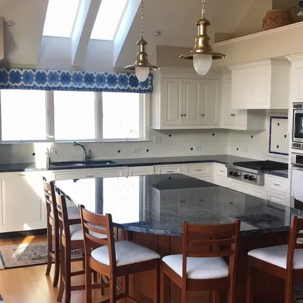 Bright, white kitchen with island, blue patterned valance, and wood bar stools.