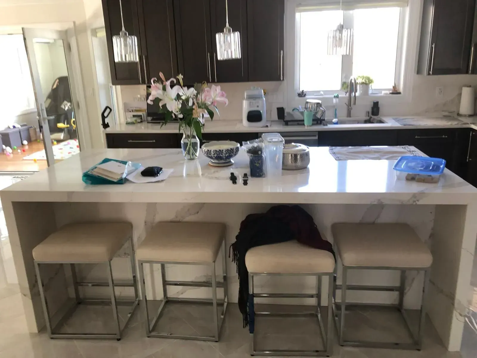 Kitchen with white countertop island, four stools, dark cabinets, and a window.