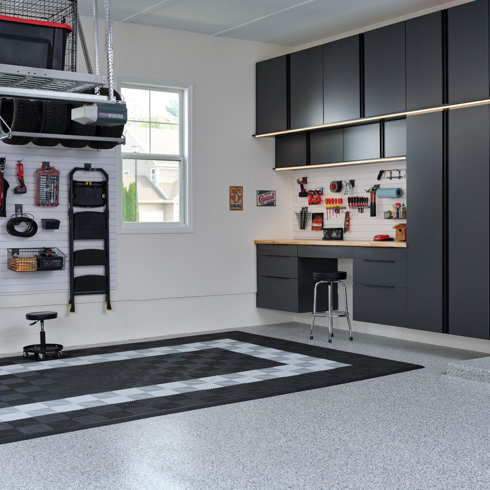Modern garage with gray cabinets, wall tools, workbench, and a large black-and-gray floor rug