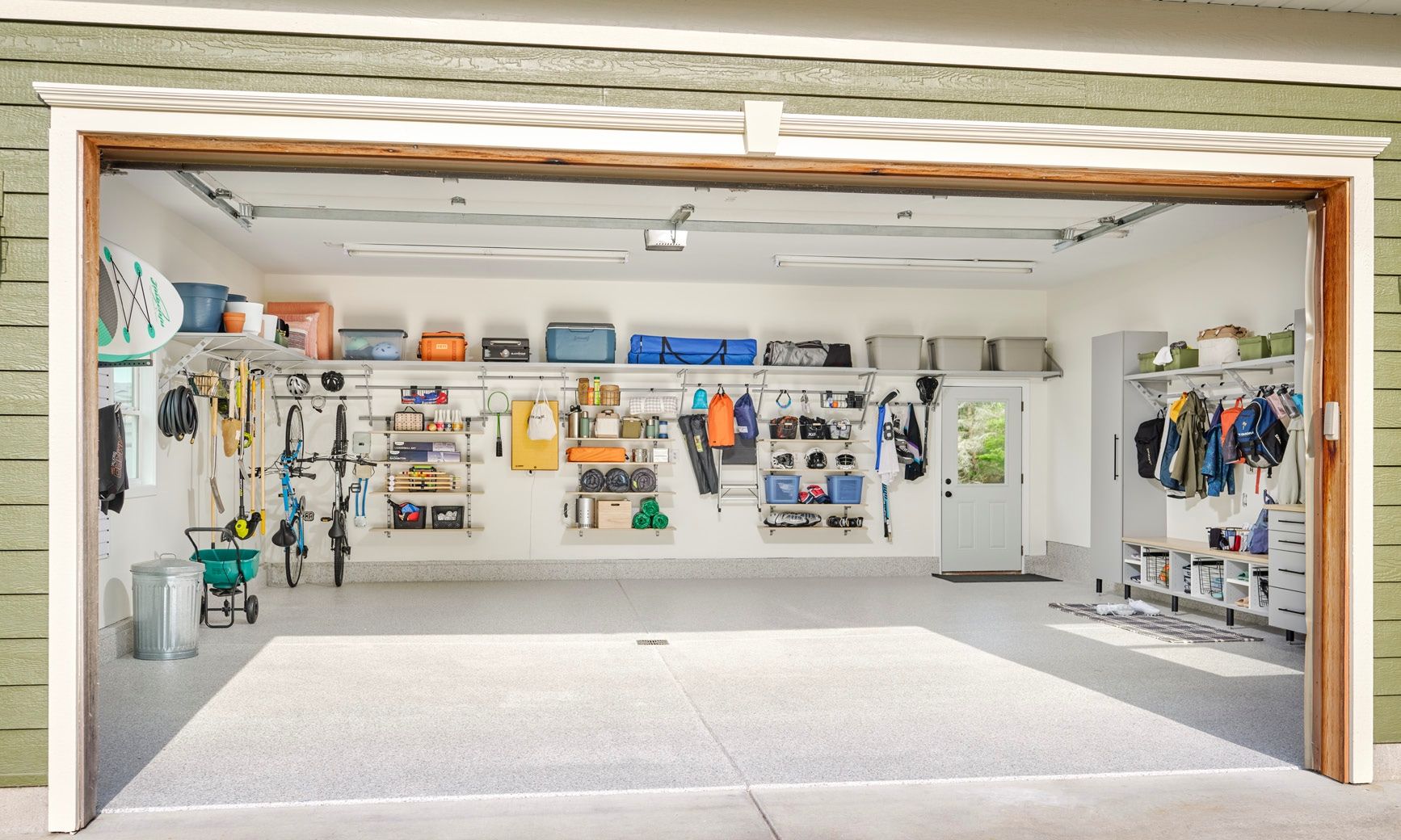 Open garage workshop with tools, shelves, and equipment on white walls, brightly lit and organized.