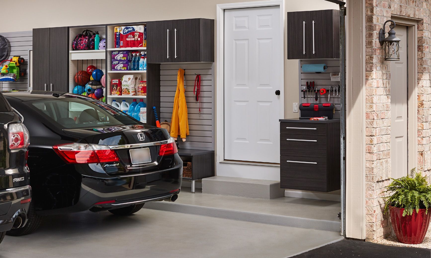 Black sedan parked in a tidy garage with gray cabinets, shelves, and a white side door