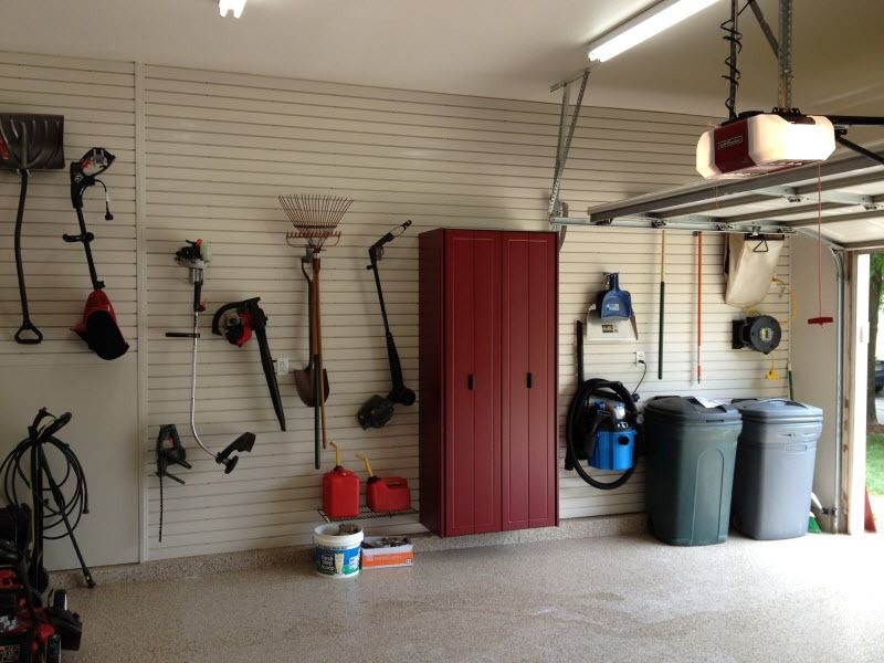 Garage wall with hanging garden tools, red cabinets, trash bins, and a garage door opener
