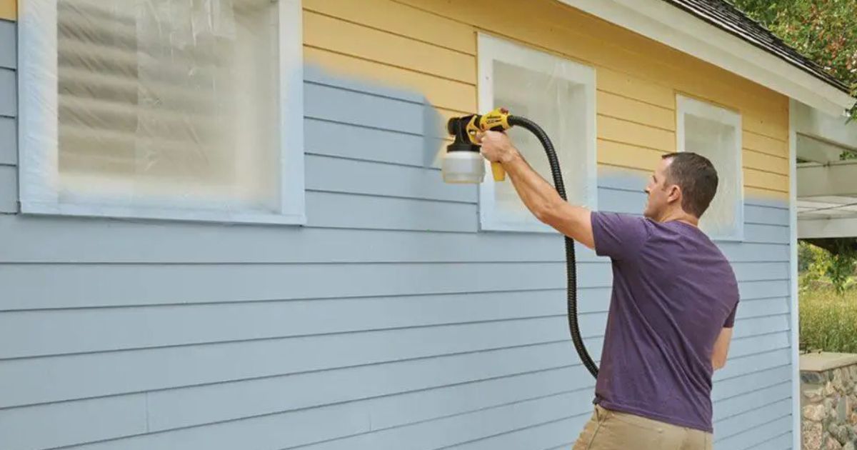 Man spraying the exterior of a yellow and blue house with a power washer