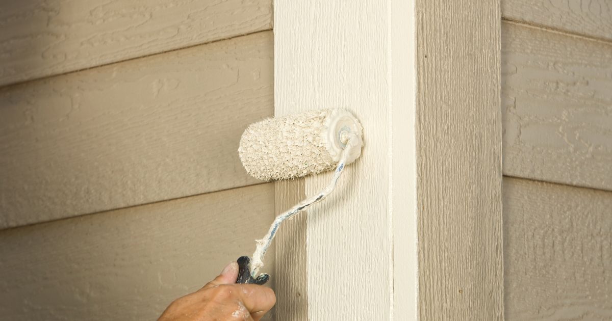Person painting a beige house trim with a roller brush