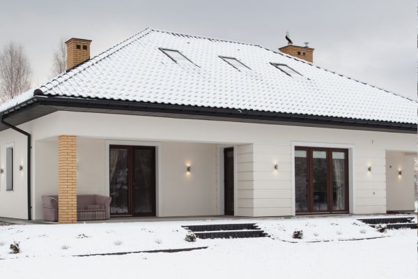 Snow-covered modern white house with dark roof and large windows