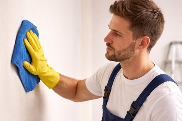 Man in blue overalls wiping a wall with a blue cloth and yellow gloves
