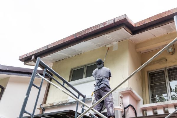 Worker painting a building exterior from a metal scaffolding platform