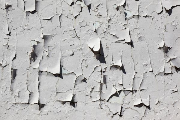 Close-up of peeling white paint on a cracked wall surface.