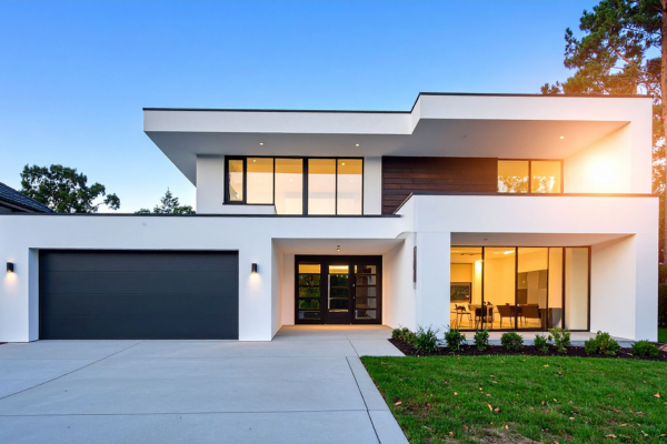 Modern two-story white house with a black garage door, large windows, and a front lawn at dusk