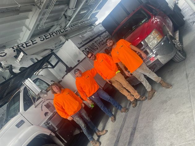 Four people in bright orange work shirts stand in a line next to two large work trucks in a garage.