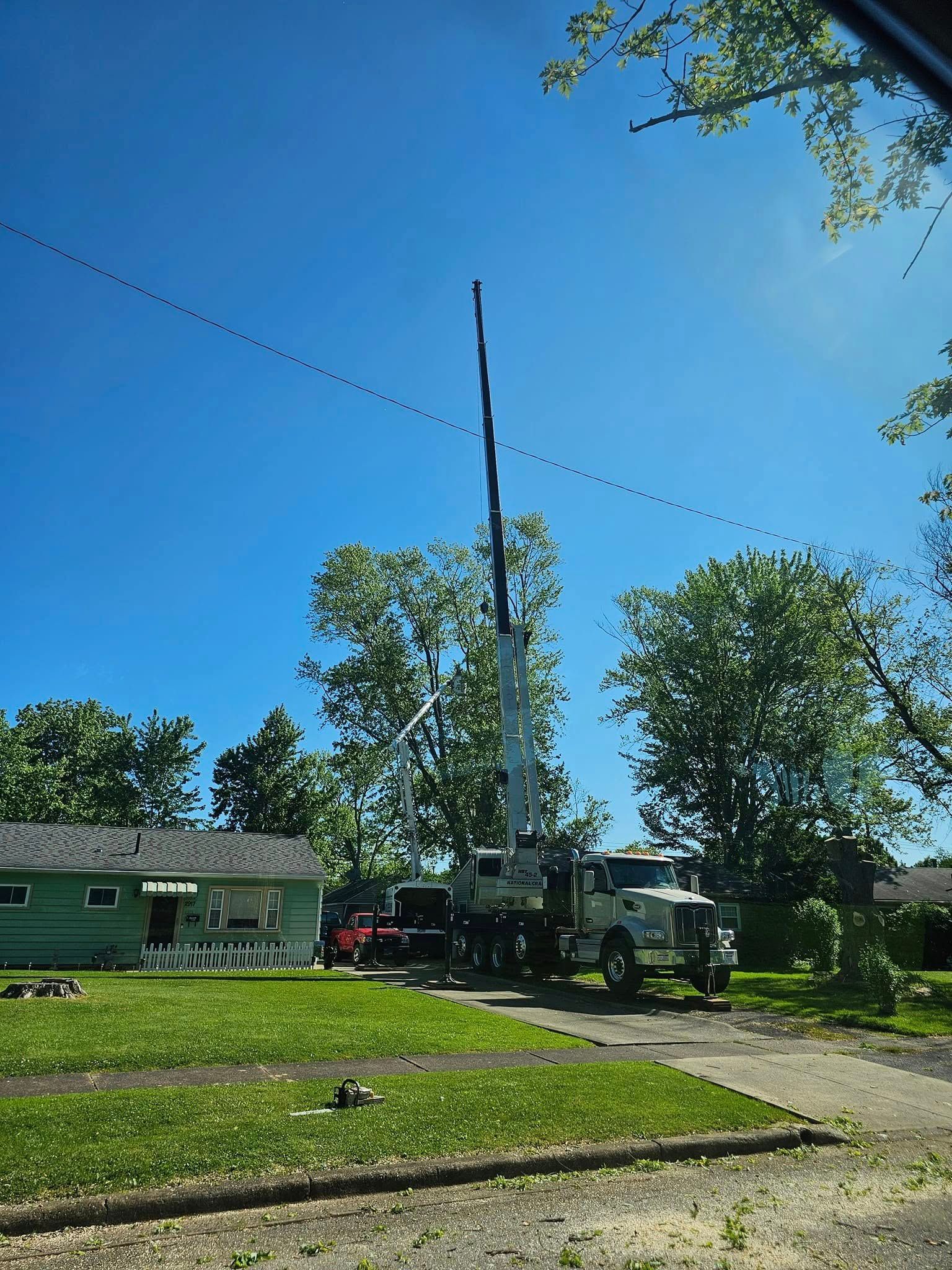 A white utility truck with an extended boom arm parked on a residential lawn under a bright blue sky.