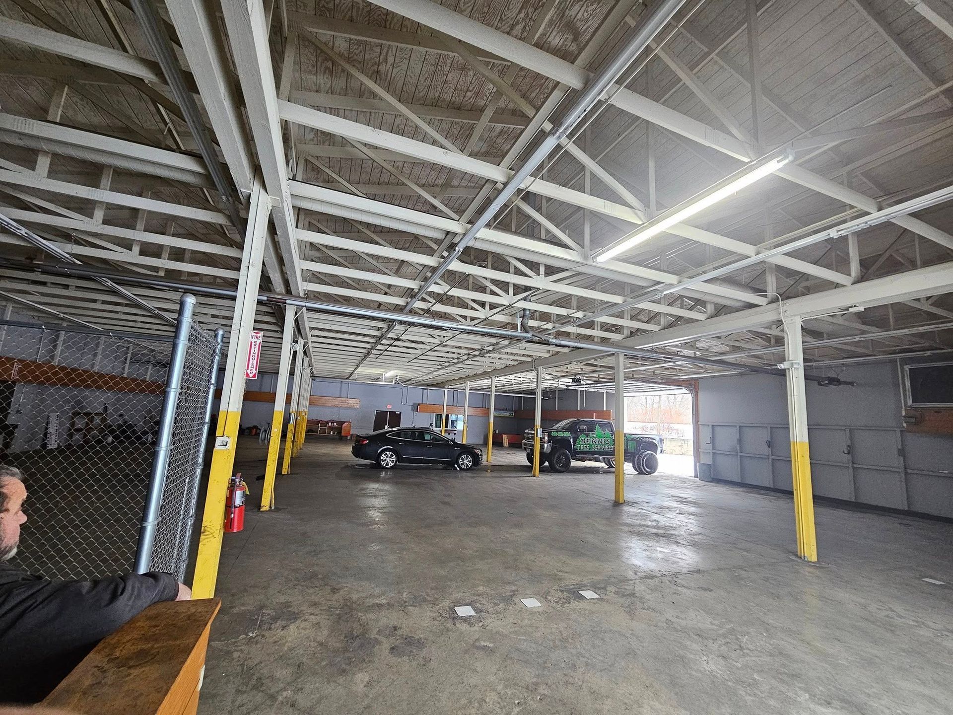 An open, industrial warehouse with exposed white trusses, a concrete floor, support beams, and two parked trucks.