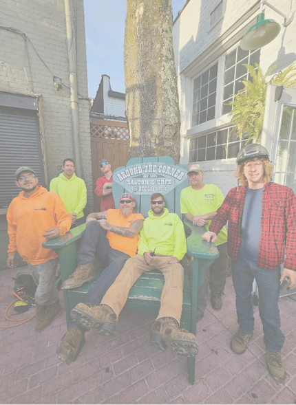 A group of people wearing work clothing and high-visibility gear pose around a large green chair in an outdoor space.