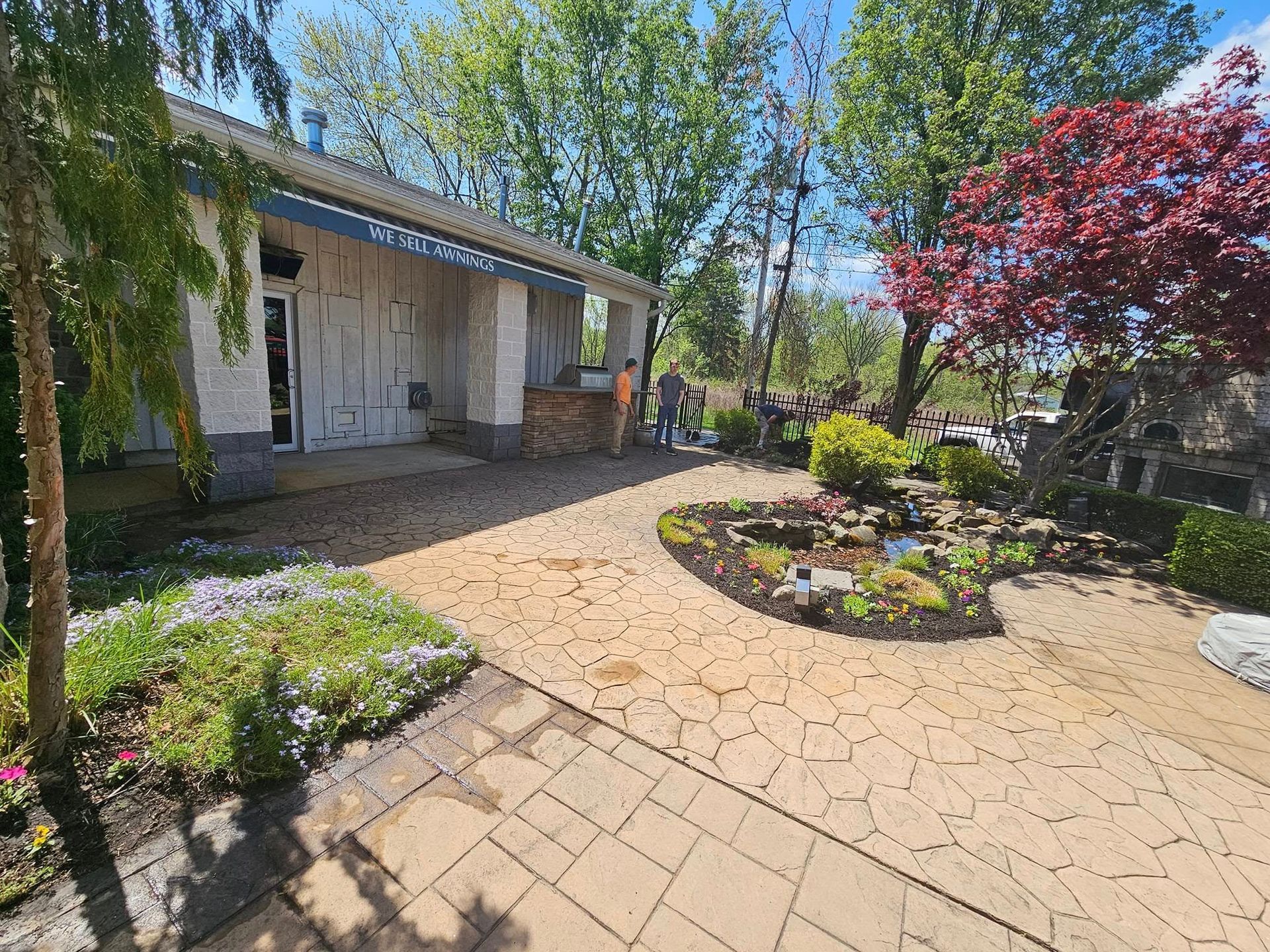 A sunny outdoor courtyard with stone pavers, a small pond, landscaping, and a white building with pillars.