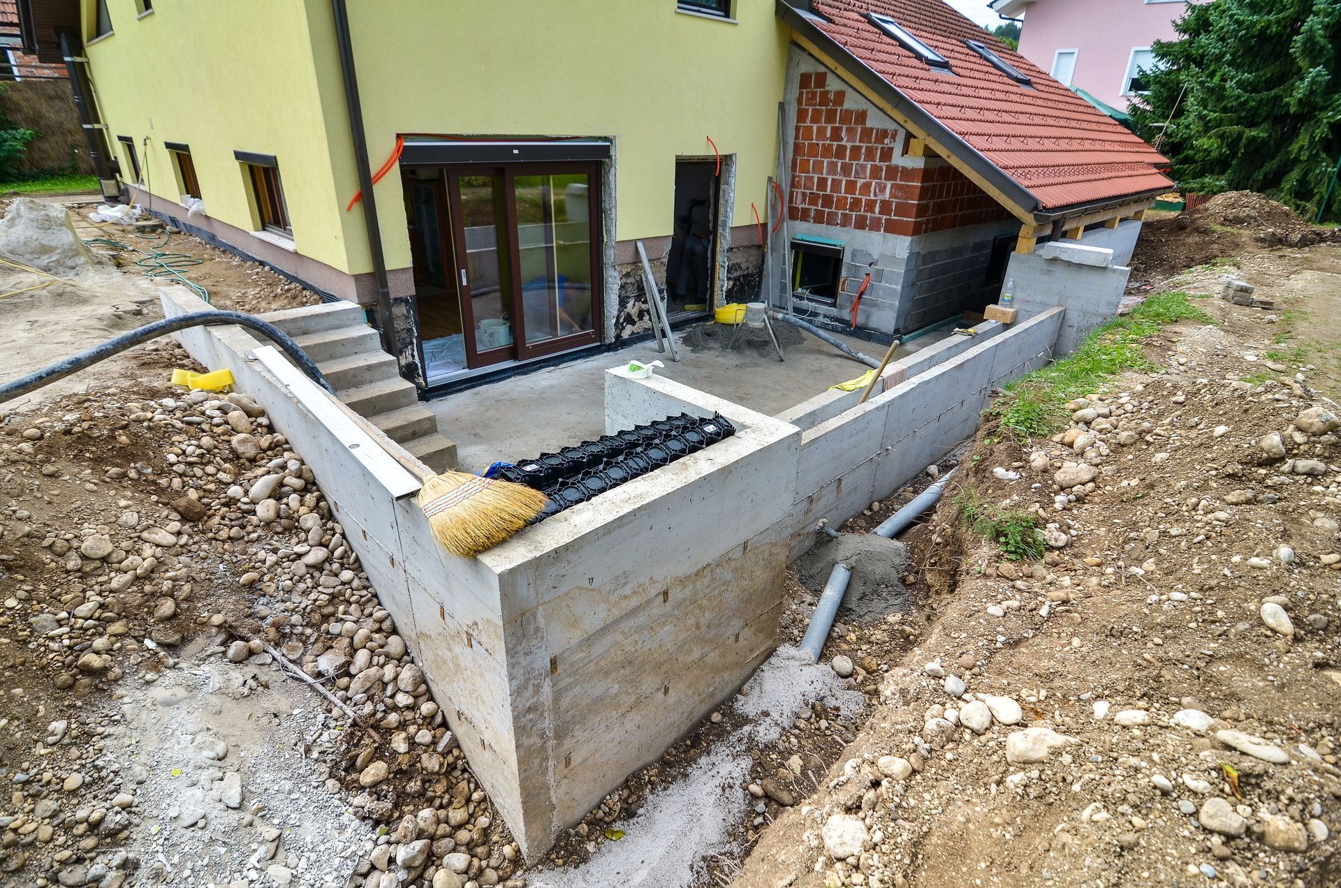 House with new concrete retaining wall and unfinished patio area on a sloped gravel lot