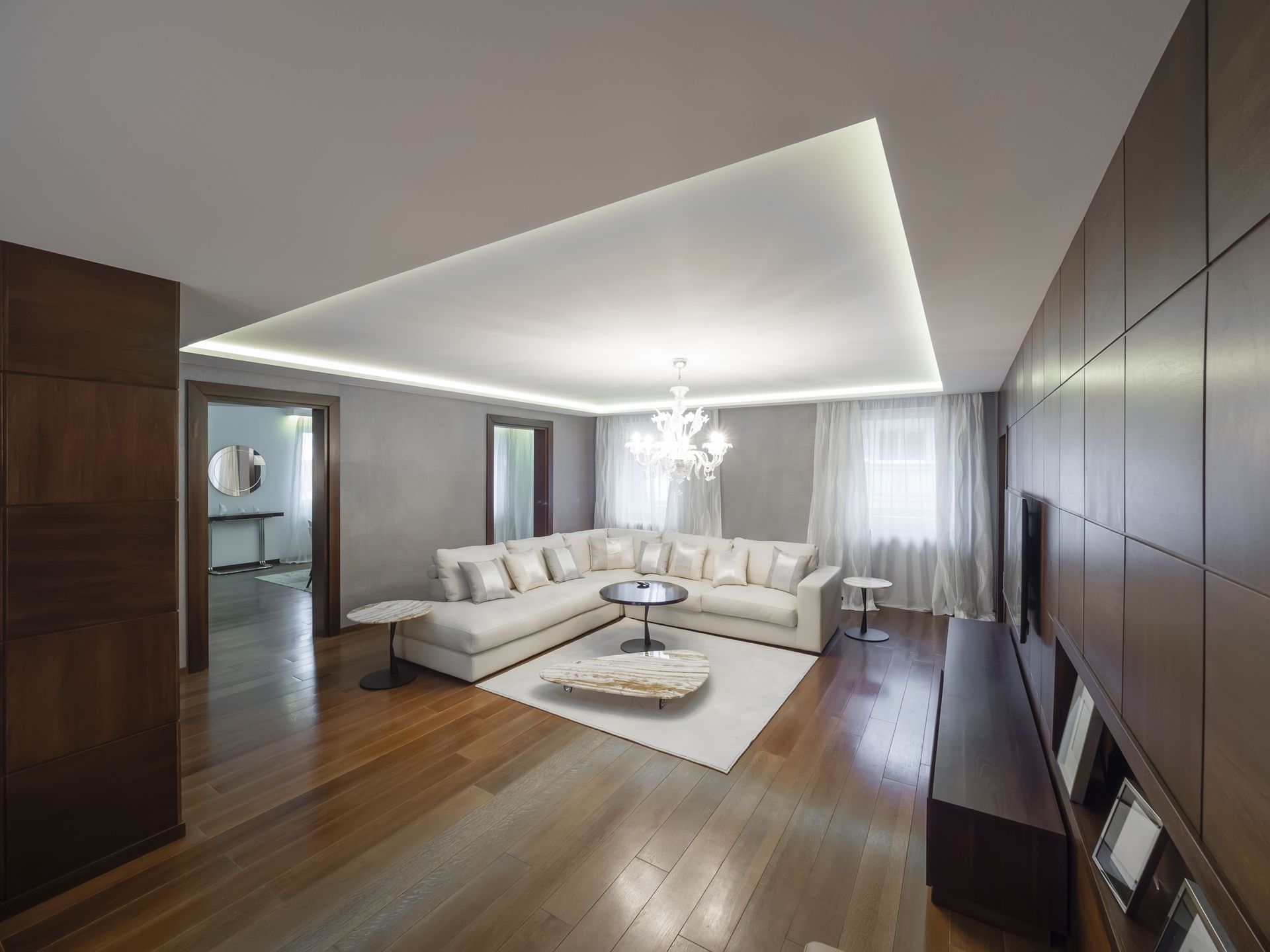 Modern living room with white sectional sofa, wood flooring, and recessed lighting.