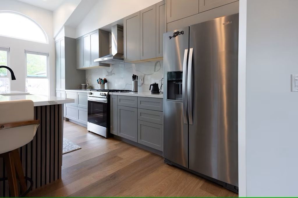 Modern kitchen with gray cabinets, stainless steel appliances, and wood flooring.
