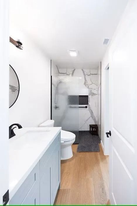 Modern bathroom with light blue vanity, marble shower, and wood floor.