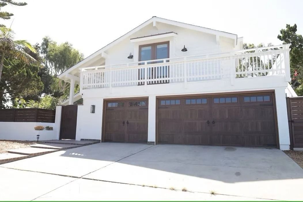 White two-story house with dark brown garage doors, a balcony, and a concrete driveway.