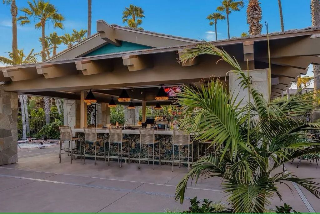 Outdoor bar with a stone facade, stools, and palm trees.