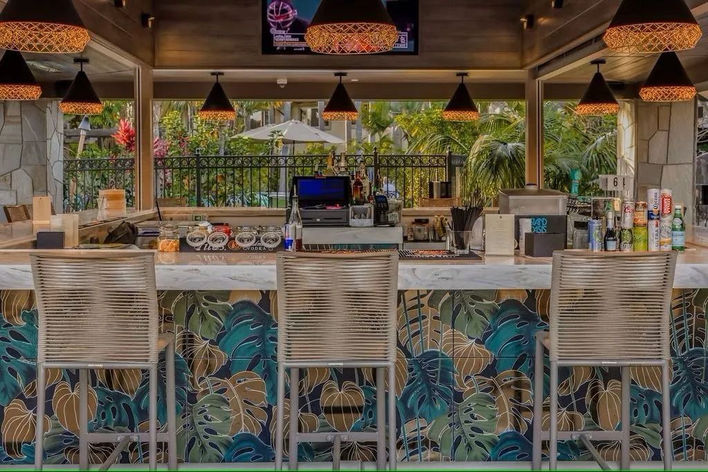 Outdoor bar with stools and jungle-themed mural, under hanging lamps.