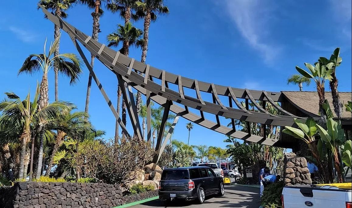 SUV driving under an architectural shade structure, tropical setting with palm trees.