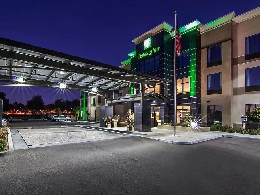 Holiday Inn hotel exterior at night, green signage, canopy over entrance, illuminated.