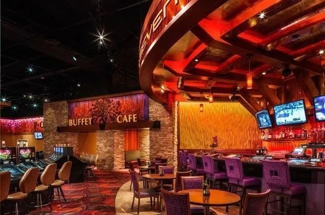 Casino buffet cafe with bar, tables, chairs, and slot machines. Rich red and gold decor.