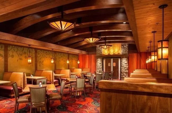 Restaurant interior with wooden beams, booths, tables, and decorative lighting.