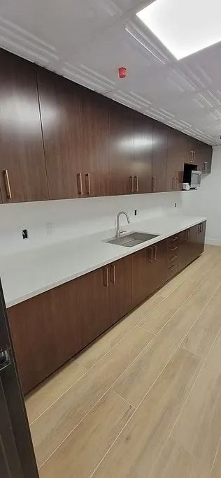 A kitchen area with brown cabinets, white countertop, and a stainless steel sink. Light wood floor.