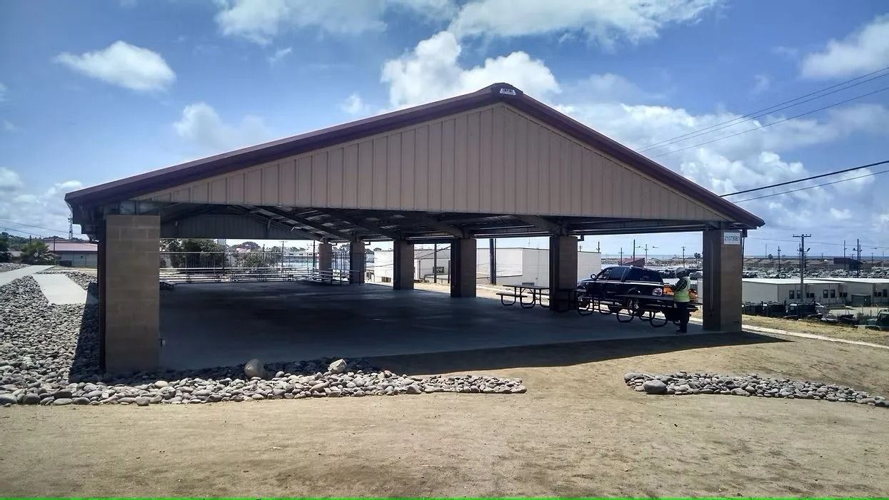 Open-air pavilion with concrete floor and metal roof, on a sunny day.