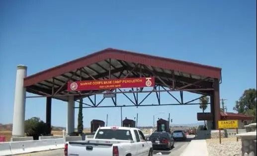 Military base entrance under a red canopy; vehicles enter, sunny day.