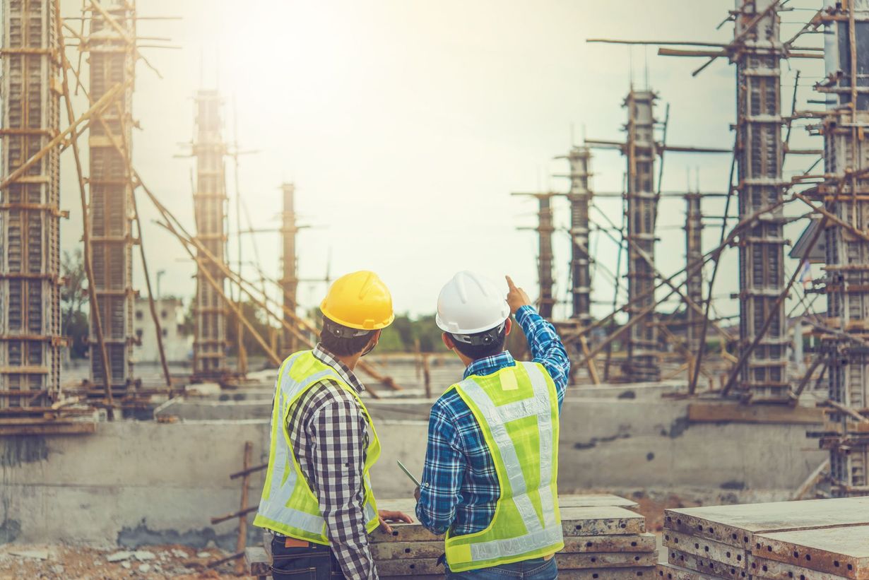 Two construction workers wearing safety vests and helmets, inspecting a construction site.