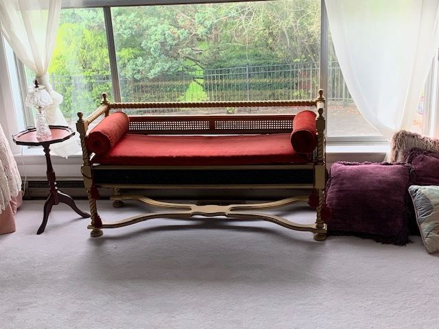 Red upholstered bench in a bright room with large windows, white curtains, and purple floor cushions