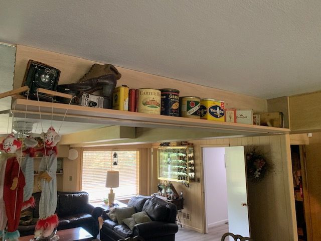 Living room with a large overhead shelf storing cans and household items above a sofa and window.