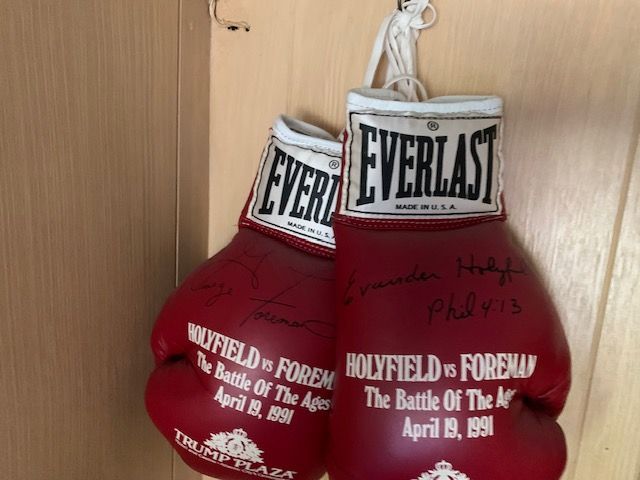 Pair of red Everlast boxing gloves with white wrists hanging against a wooden wall.