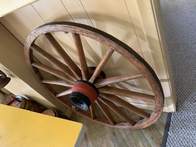 Large wooden wagon wheel leaning against a beige wall indoors near a yellow cabinet.