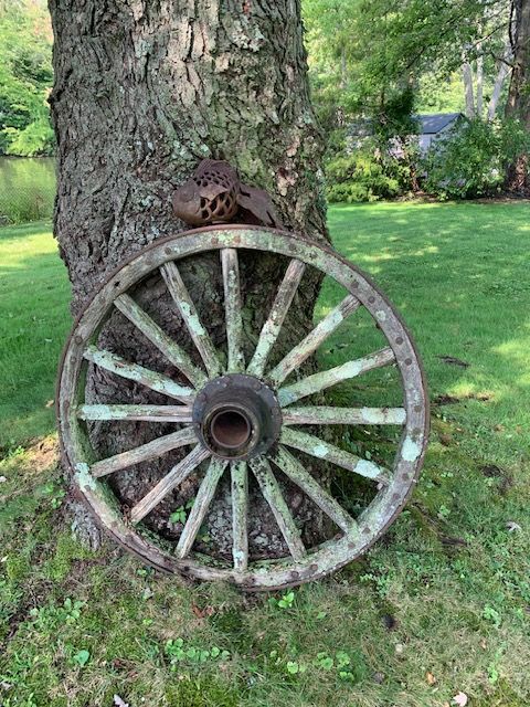 Old wooden wagon wheel leaning against a tree in a grassy yard