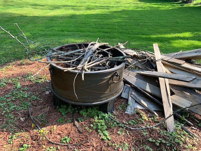 Metal fire pit filled with branches and scrap wood on grass in a yard