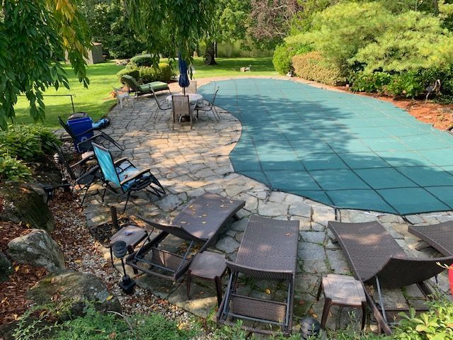 Backyard patio with a covered pool, stone fire pit, and lounge chairs in a lush garden