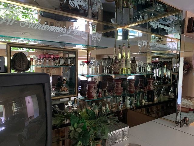 Mirrored restaurant interior with a bar, shelves of bottles, and a TV in the foreground.