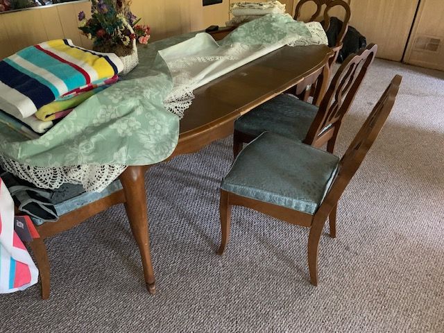 Dining table with cloth and chair in a carpeted room, with pillows and flowers on top