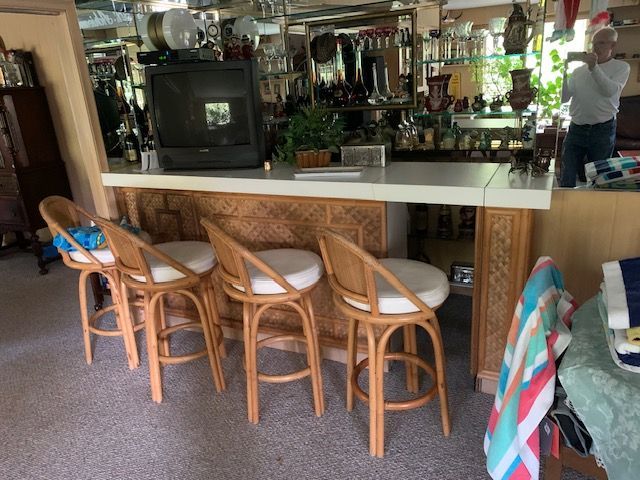 Cozy home bar with wicker stools, shelves of bottles, and a person reflected at the counter