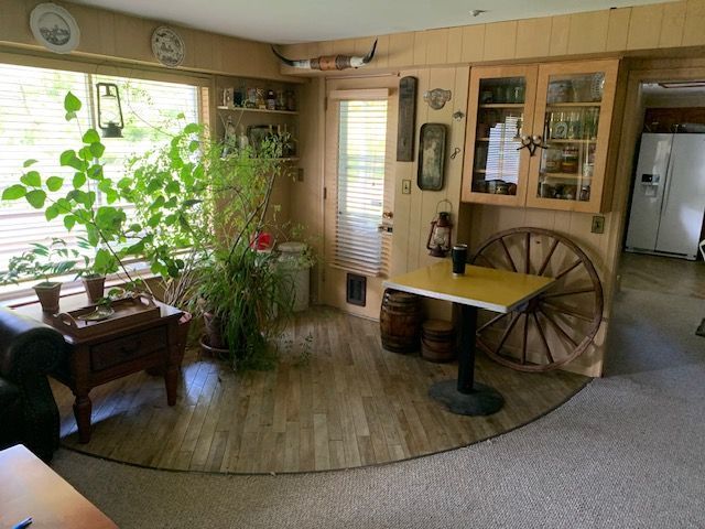 Cozy sunlit living room with plants, wood furniture, and a decorative wagon wheel table