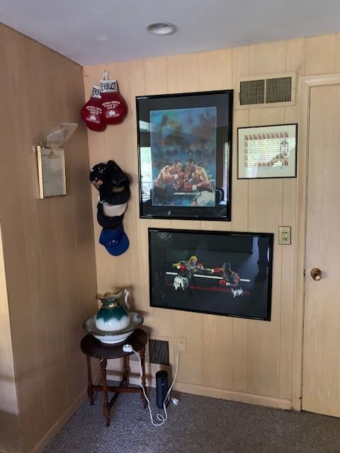 Hallway wall with framed art, hanging hats, a small table with a lamp, and a door on the right.