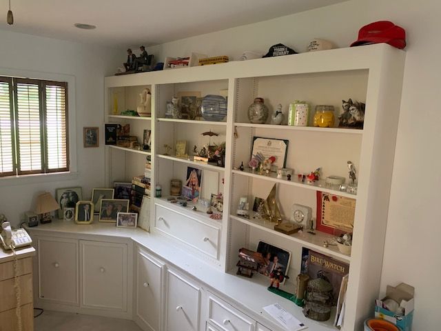 White built-in shelves and cabinets in a bright room, displaying framed photos, decor, and small collectibles.