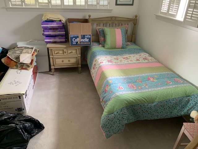 Small bedroom with a single bed, nightstand, and stacks of folded blankets by the window.