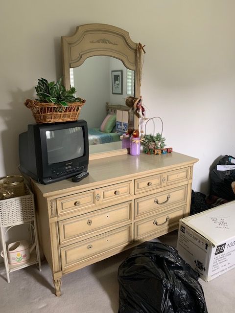 Vintage dresser with mirror, small TV, plants, and boxes in a bedroom corner