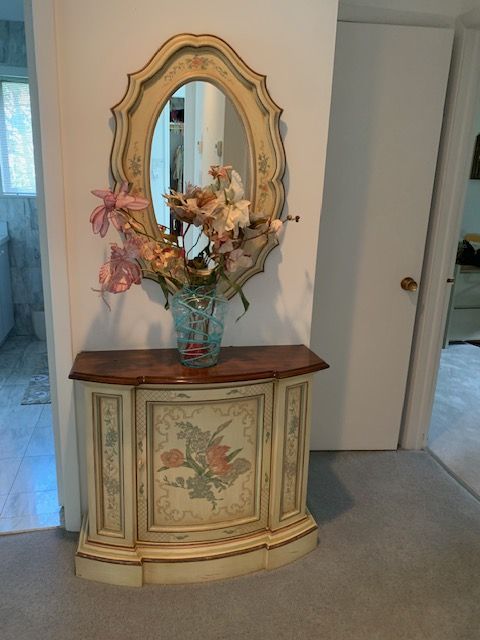Decorative antique cabinet with flowers, beneath an ornate mirror in a hallway